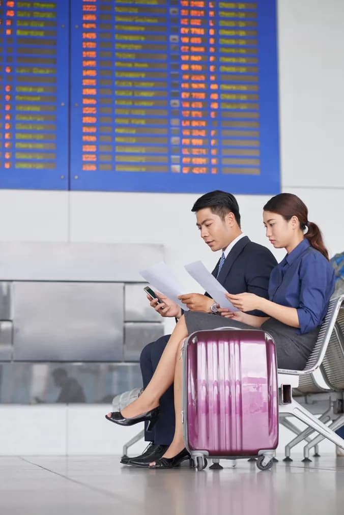 Travelers waiting beneath a departure board with their luggage