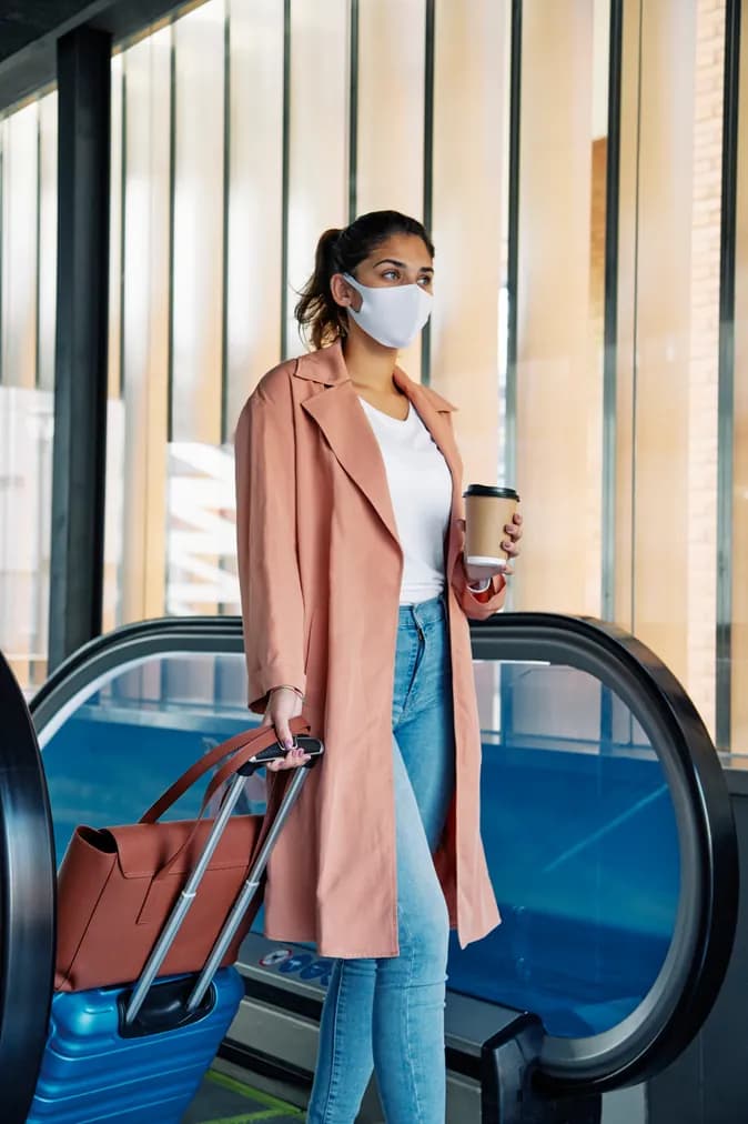 A traveler riding an escalator with her luggage and coffee