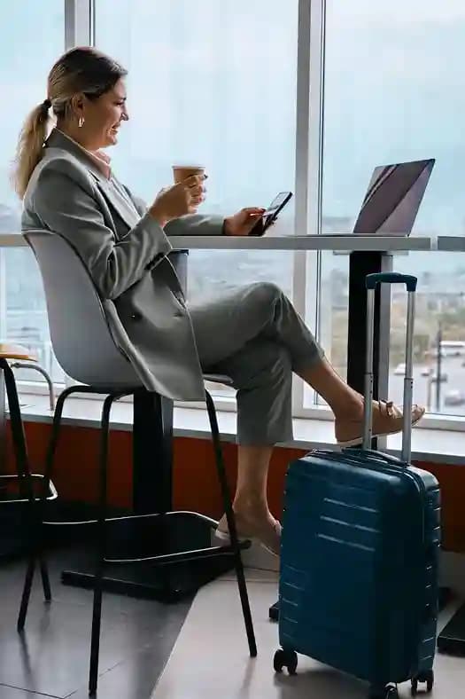 A traveler working at a terminal counter beside her cabin bag