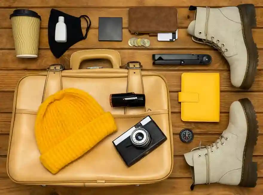 An open suitcase with a camera, hat, boots and travel accessories arranged around it