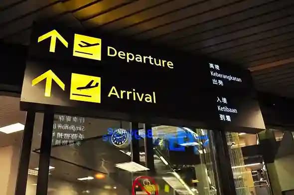 Illuminated airport signage pointing to Departure and Arrival in several languages