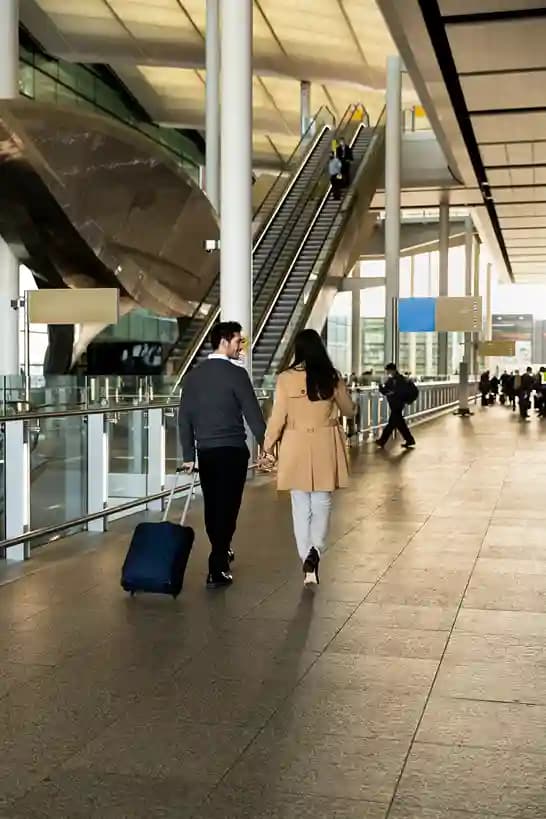 A couple walking through a terminal concourse with a suitcase toward the escalators