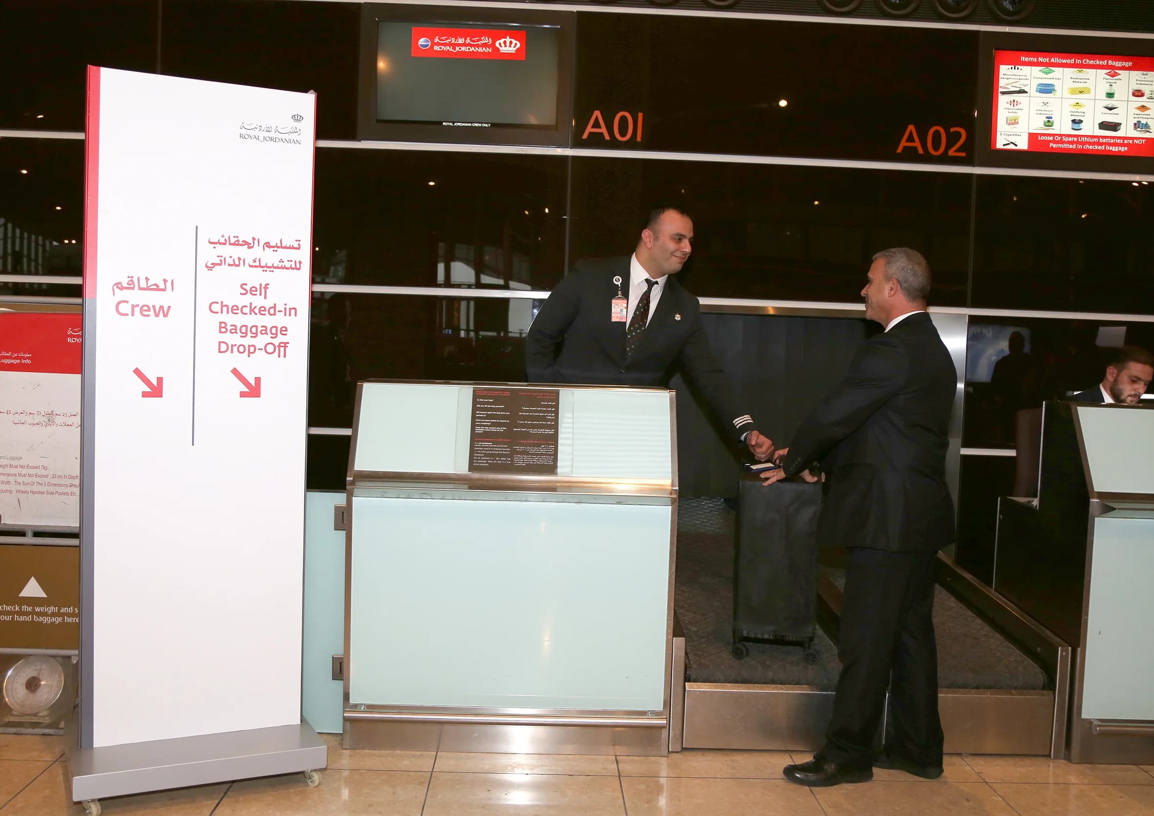 An airport agent greeting a traveler at a check-in and baggage drop counter